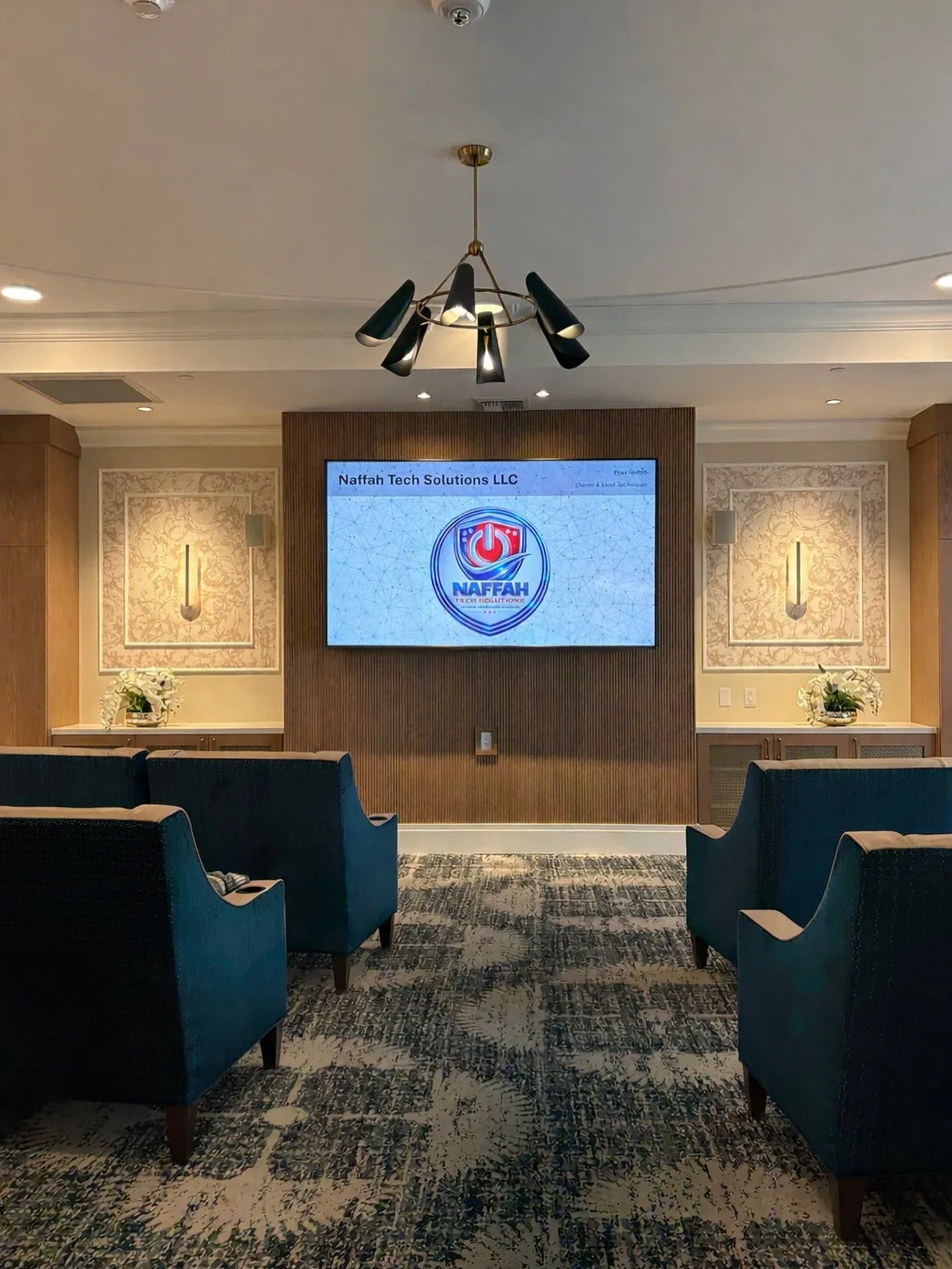 Modern office lobby with blue chairs facing a wall-mounted screen displaying Naffah Tech Solutions logo.