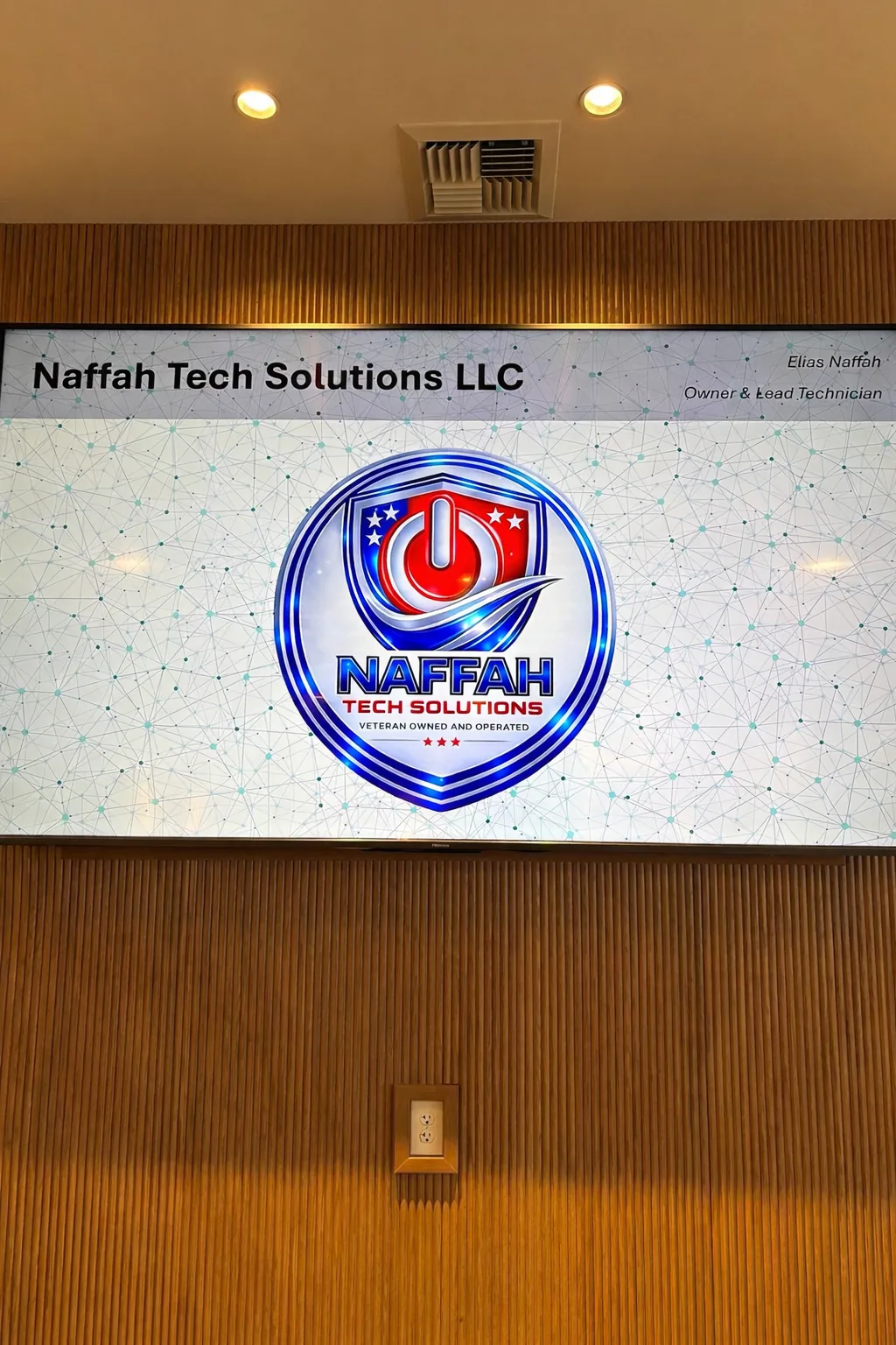 Naffah Tech Solutions LLC illuminated sign with blue and red power button logo on office wall.
